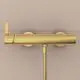 Brausearmatur in gebürstetem Gold an einer hellen Wand montiert, gestaltet von Ideal Standard. Die Armatur hat eine glatte Oberfläche und ist funktional angeordnet.